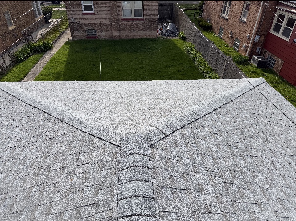 Completed gray shingle roof ridge overlooking a green backyard